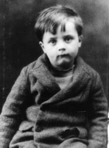 A young boy wearing a sweater and sitting in a chair.