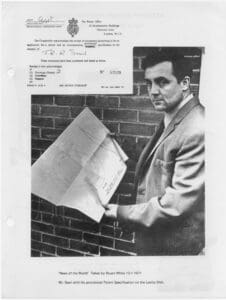 A man holding an envelope in front of a brick wall.